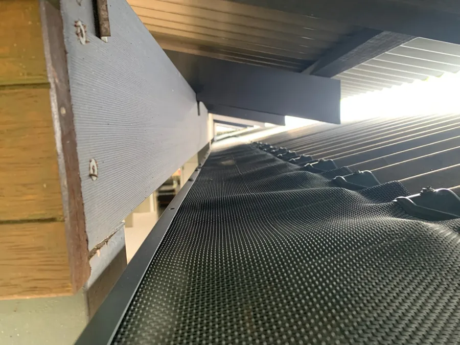 Close view along a gutter fitted with fine metal ember mesh, fixed with screwed clips under the eaves